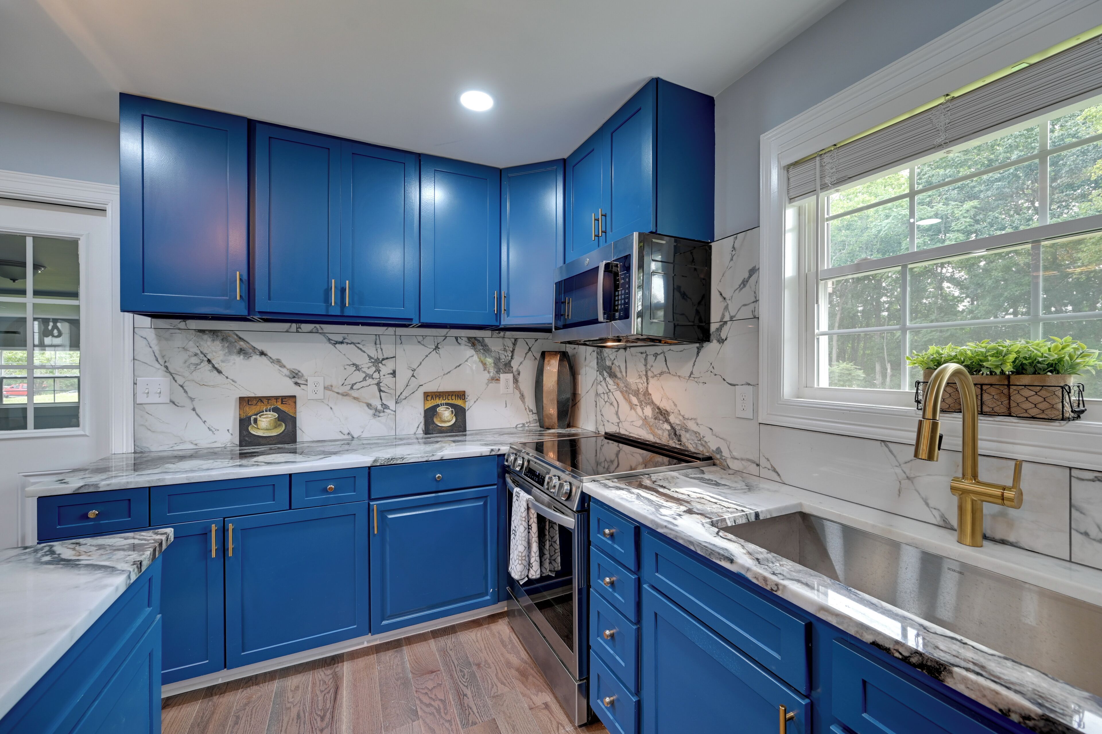 A kitchen with blue cabinets, a stainless steel oven, and a marble countertop.