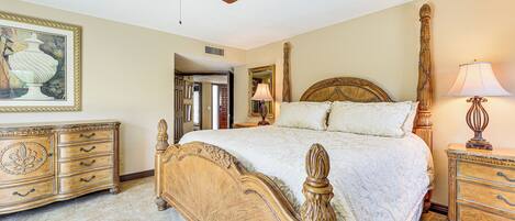 A bedroom with a large bed, wooden headboard, a ceiling fan, a dresser, and a framed picture on the wall.