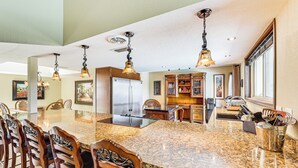 A spacious kitchen with a large granite island, wooden chairs, and pendant lighting. - Golf, Swim & Grill: Snowbirds Escape in Sun Lakes (Chandler)