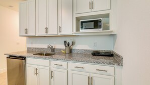 A kitchen with white cabinets, a granite countertop, a dishwasher, a microwave, and a coffee maker. - Beach-hop & Golf! Port St Lucie Apt w/ Shared Yard (Port Saint Lucie)