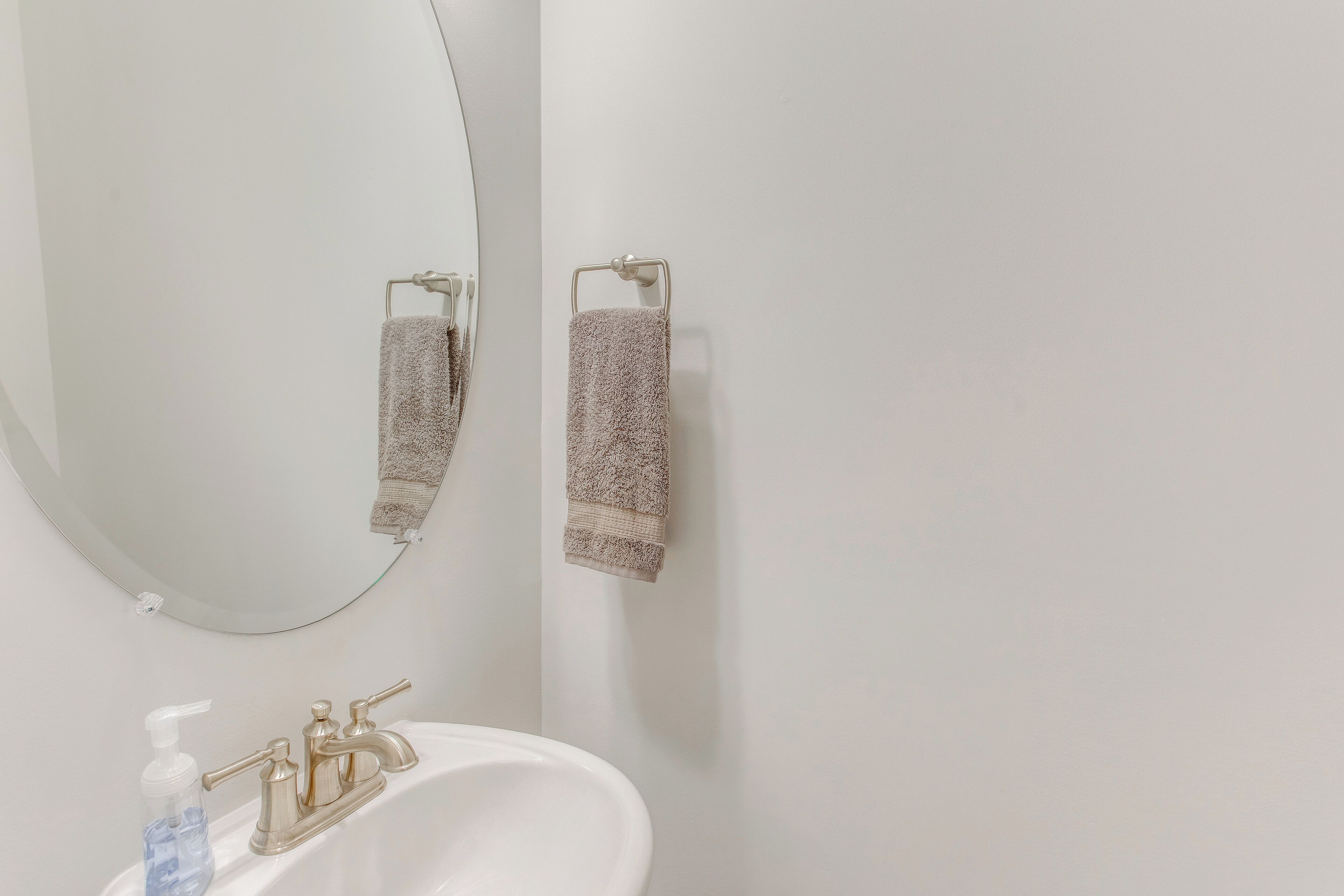 A bathroom with a white sink, a mirror, and two towels hanging on towel racks.
