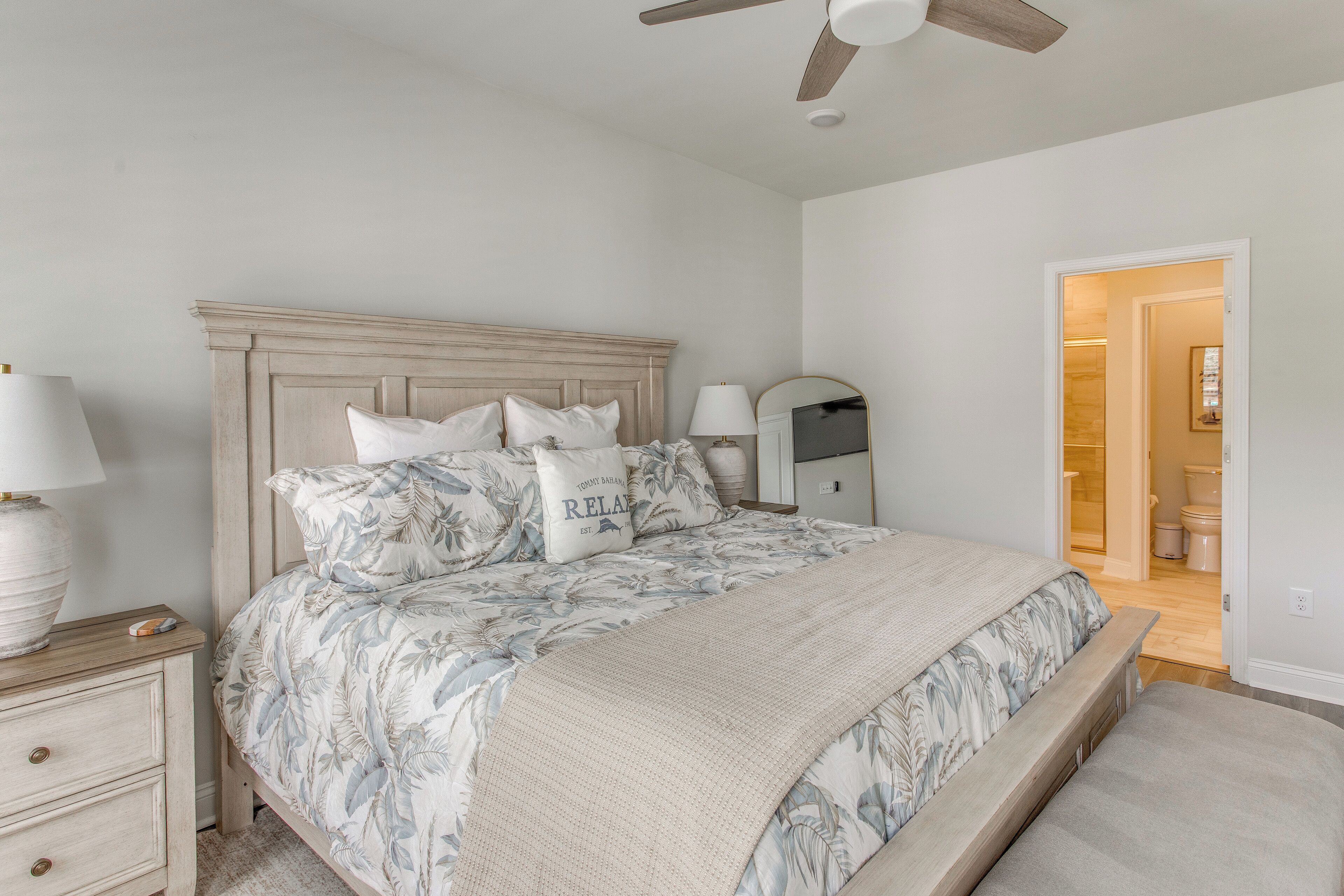 A bedroom with a bed, nightstands, a ceiling fan, and a door leading to another room.