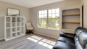 Habitación con un estante empotrado blanco, un sofá de cuero, una silla blanca y un ventanal con vistas a la vegetación.