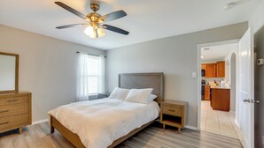 Un dormitorio con cama, mesitas de noche, ventilador de techo y vista a la cocina.