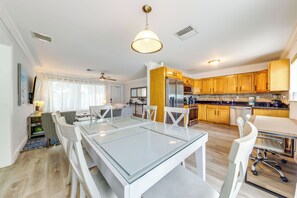 A modern kitchen with wooden cabinets, a central island, and a dining area with a glass table and white chairs. - Great for Snowbirds! Pompano Beach Home w/ Patio (Pompano Beach)