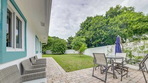 Une terrasse avec des meubles en osier et une table, une cour gazonnée et une clôture blanche.
