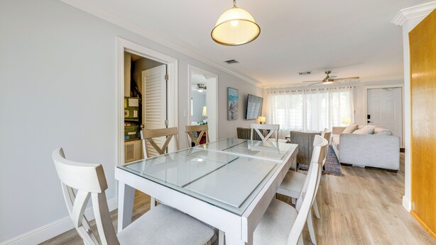 Un espace repas moderne avec une table à plateau en verre, des chaises blanches et un ventilateur de plafond.