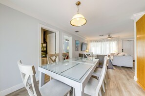 Un espace repas moderne avec une table à plateau en verre, des chaises blanches et un ventilateur de plafond.