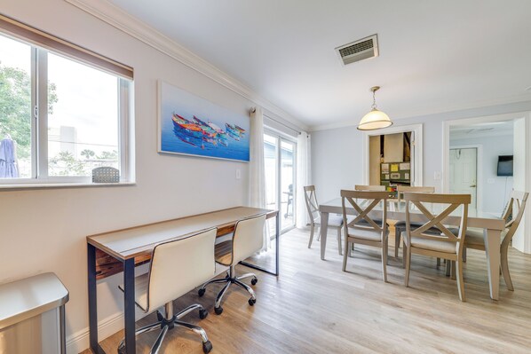 Un espace repas moderne avec une table et des chaises en bois, une grande fenêtre avec des rideaux et un tableau au mur.