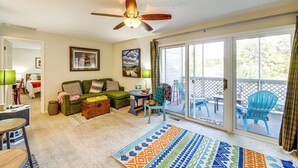 A cozy living room with a ceiling fan, a green sofa, a patterned rug, and a view of a balcony with outdoor furniture. - 3 Mi to IU: Dog-friendly Condo w/ Pool Access! (Bloomington)