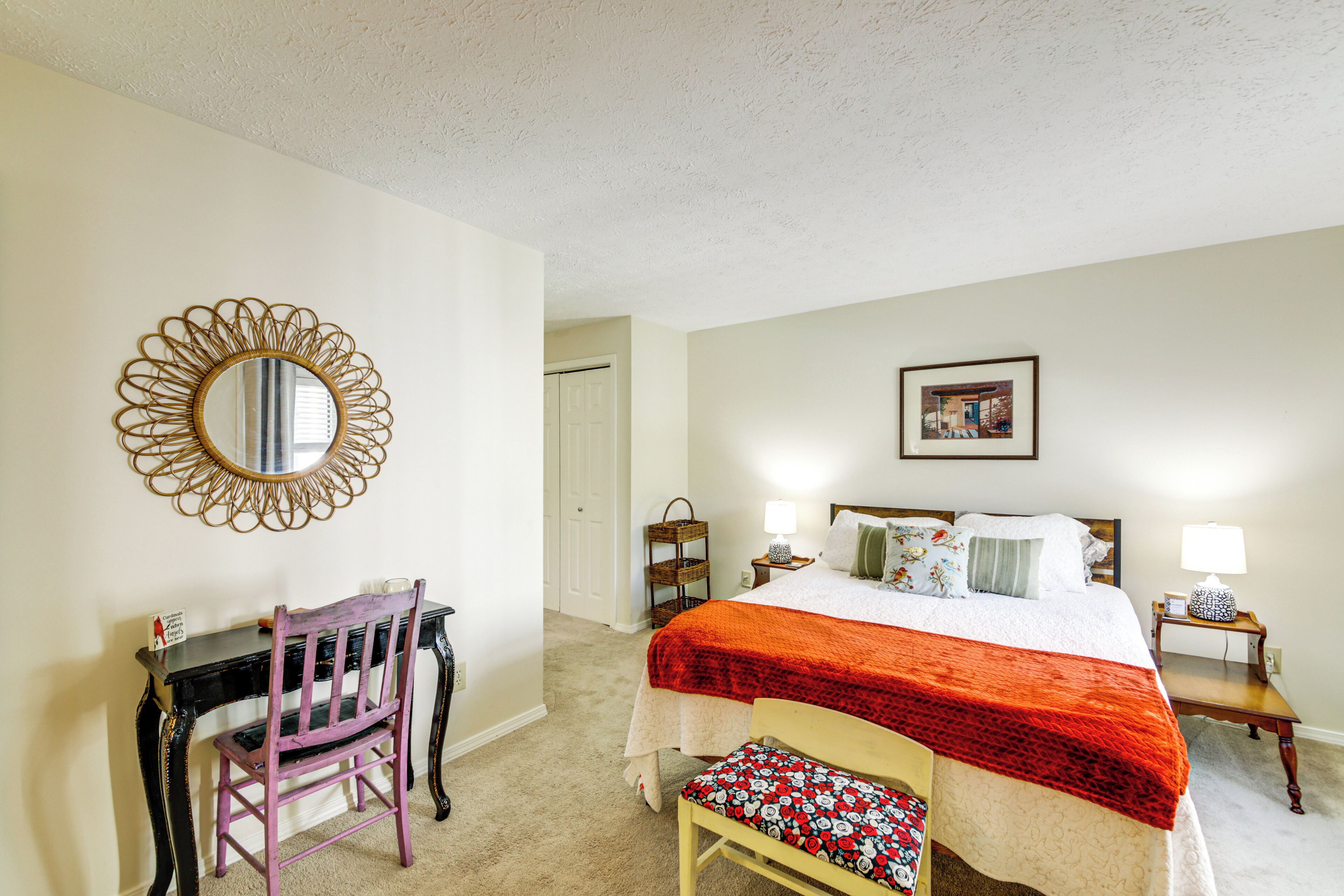 A bedroom with a bed, bedside tables, a chair, a desk, and a mirror.