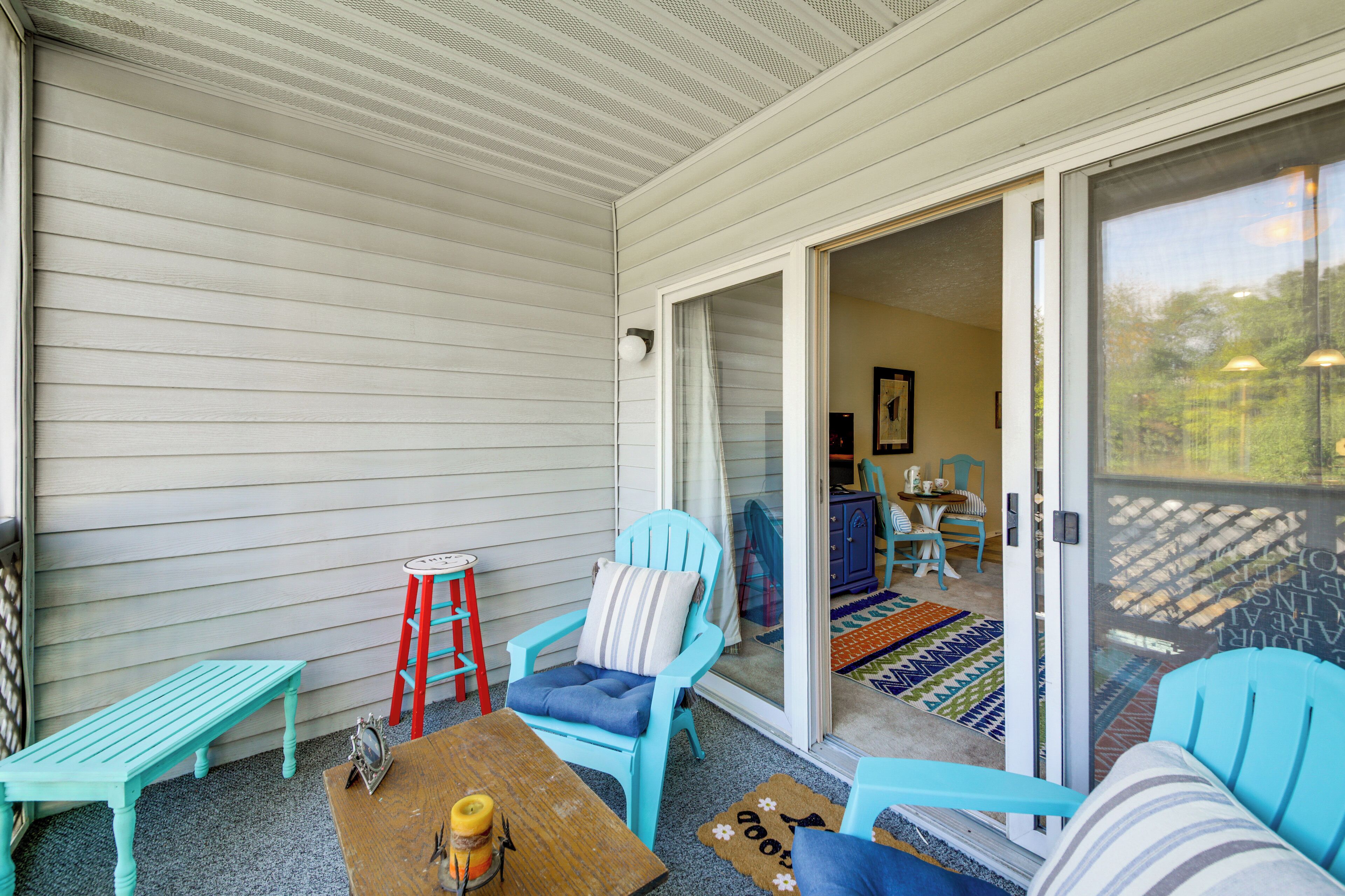Un patio couvert avec une porte-fenêtre coulissante donnant sur un espace intérieur. On y trouve deux chaises turquoise, une table en bois avec une bougie et une échelle rouge.