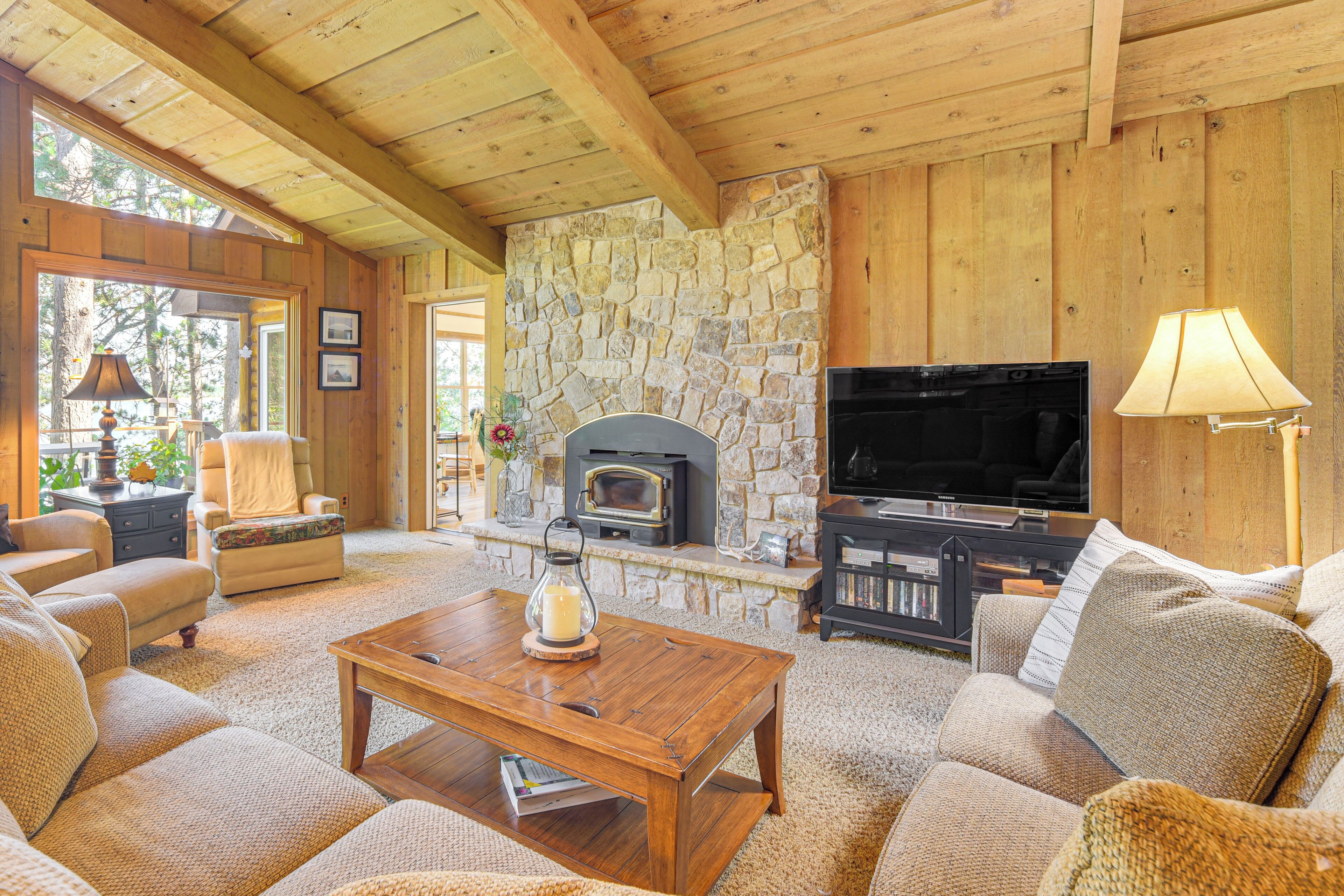 A cozy living room with a stone fireplace, wooden ceiling, and comfortable seating.