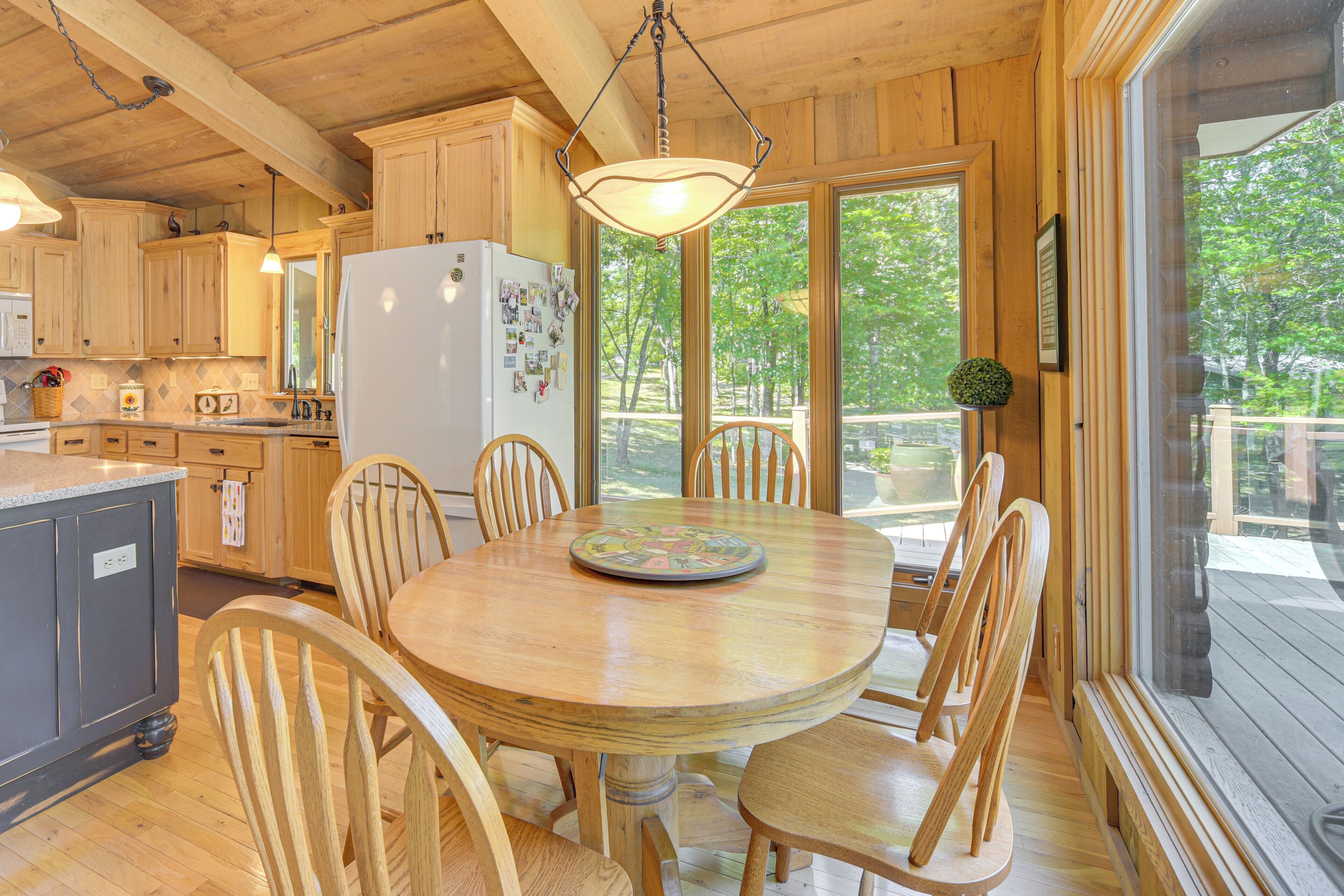A wooden interior with a round dining table surrounded by chairs, a refrigerator, and wooden cabinets.