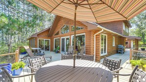 A wooden cabin with a deck, outdoor seating, and a large umbrella. - Waterfront Escape on Big Sand Lake w/ Private Dock (Minong)