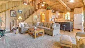 A spacious living area with a wooden ceiling, a large sofa, a coffee table, and a kitchen area with a refrigerator and microwave. - Waterfront Escape on Big Sand Lake w/ Private Dock (Minong)