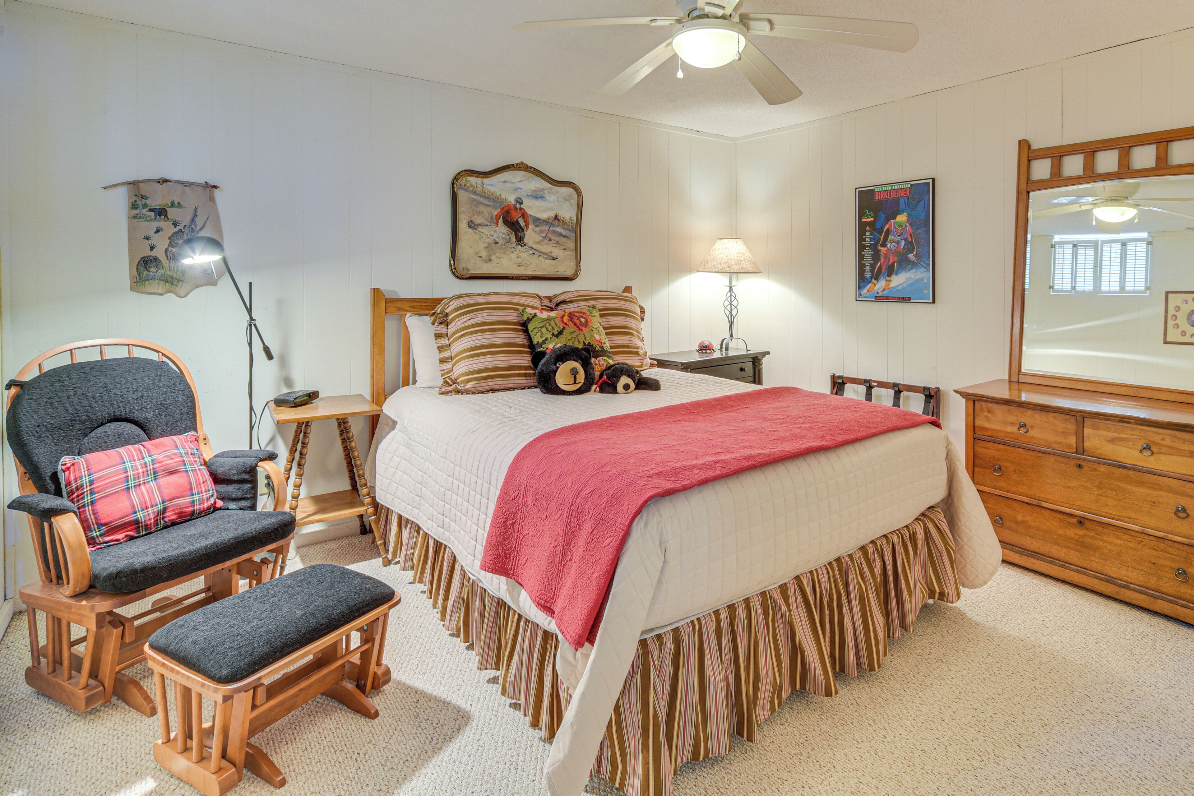 A bedroom with a bed, a chair, a desk, a lamp, a dresser, and a ceiling fan.