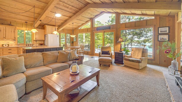 A spacious living area with a wooden ceiling, large windows, a sofa set, and a dining area. - Waterfront Escape on Big Sand Lake w/ Private Dock (Minong)