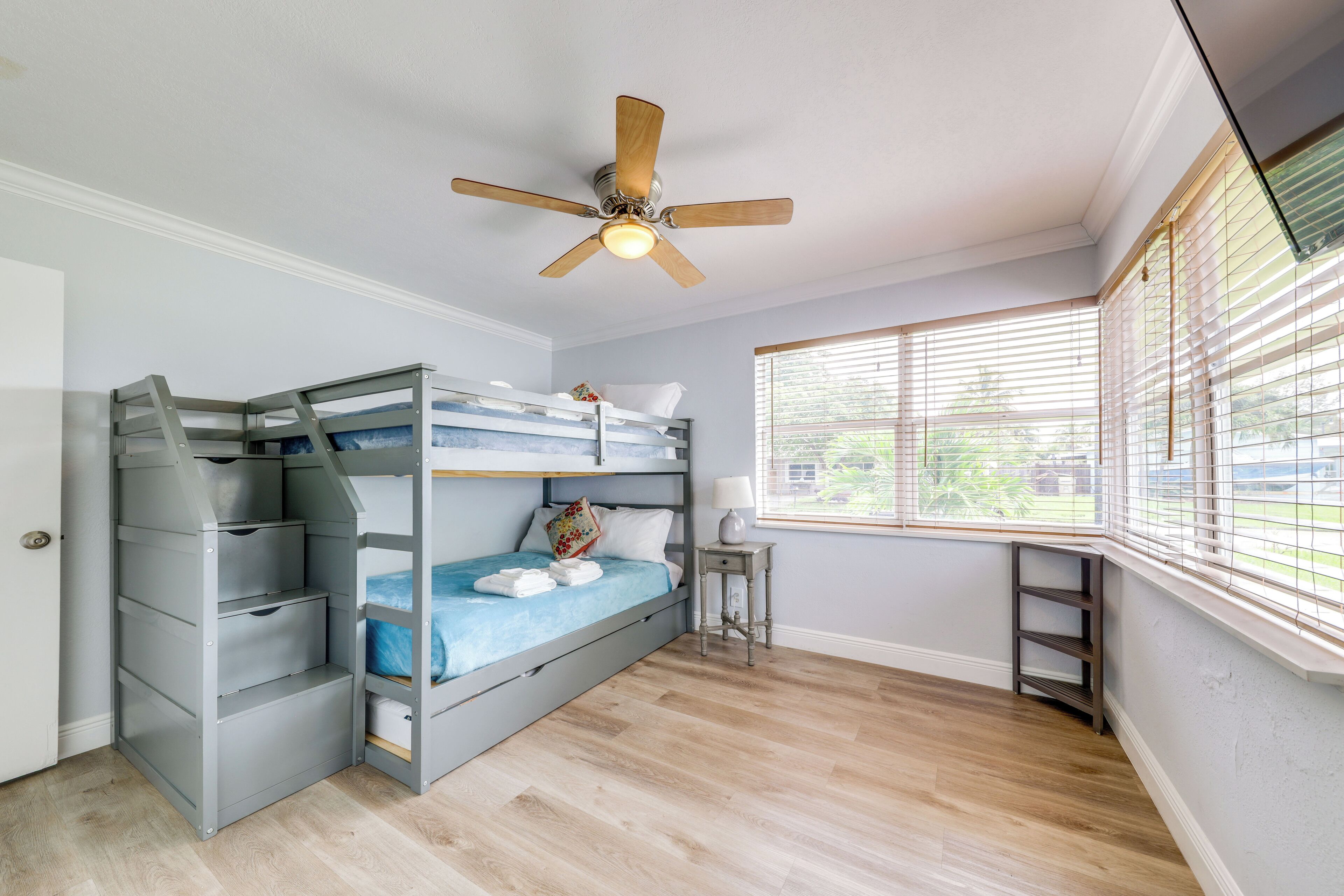 A bedroom with a bunk bed, a ceiling fan, a window with blinds, and a small table.
