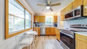 Una cucina moderna con mobili in legno, elettrodomestici in acciaio inossidabile e una zona pranzo con sedie bianche.