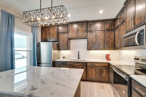 A modern kitchen with dark wood cabinets, a marble island, stainless steel appliances, and a unique chandelier. - 7 Mi to Afb: Central & Modern San Angelo Home (San Angelo)