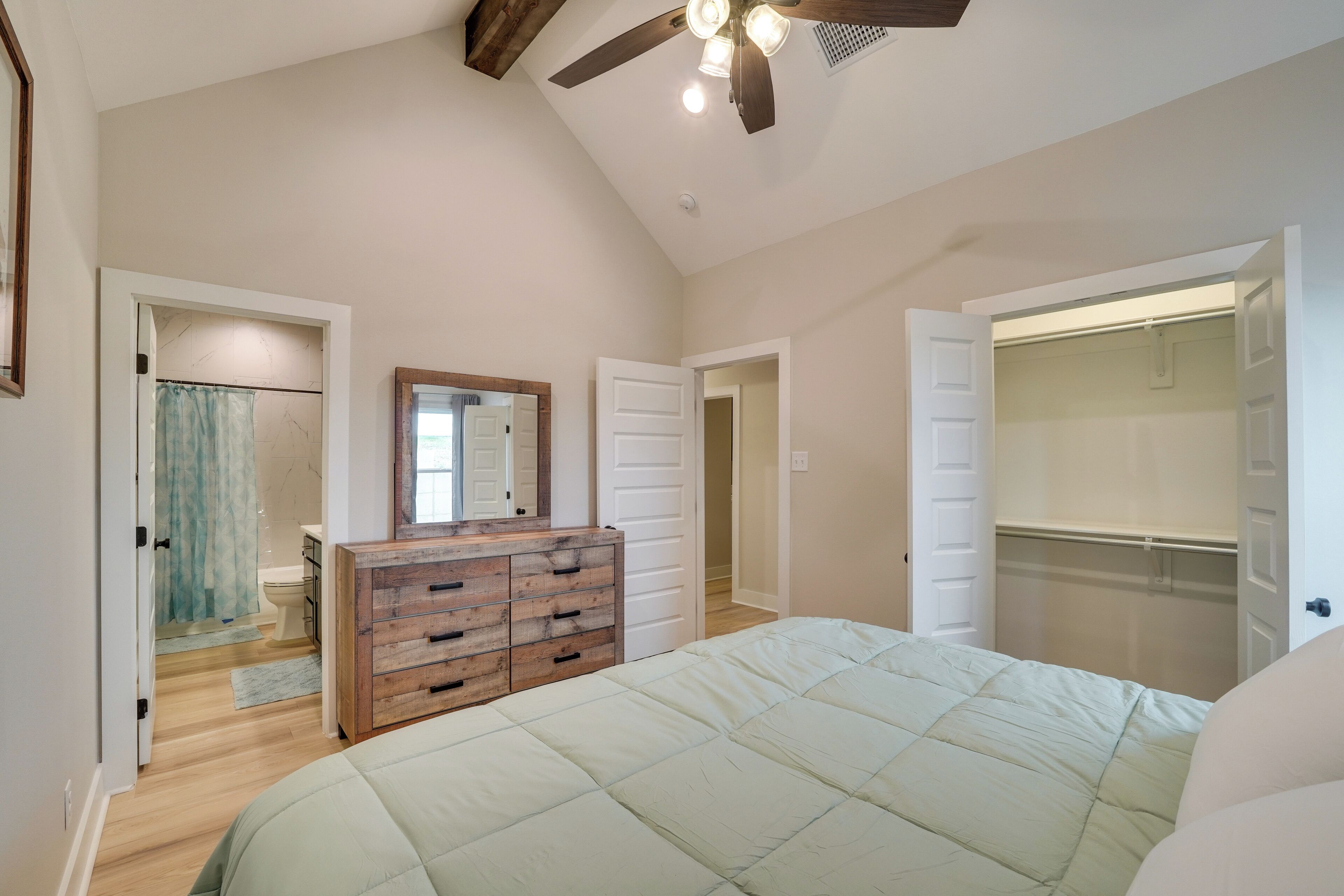 A bedroom with a bed, wooden dresser, and a walk-in closet.