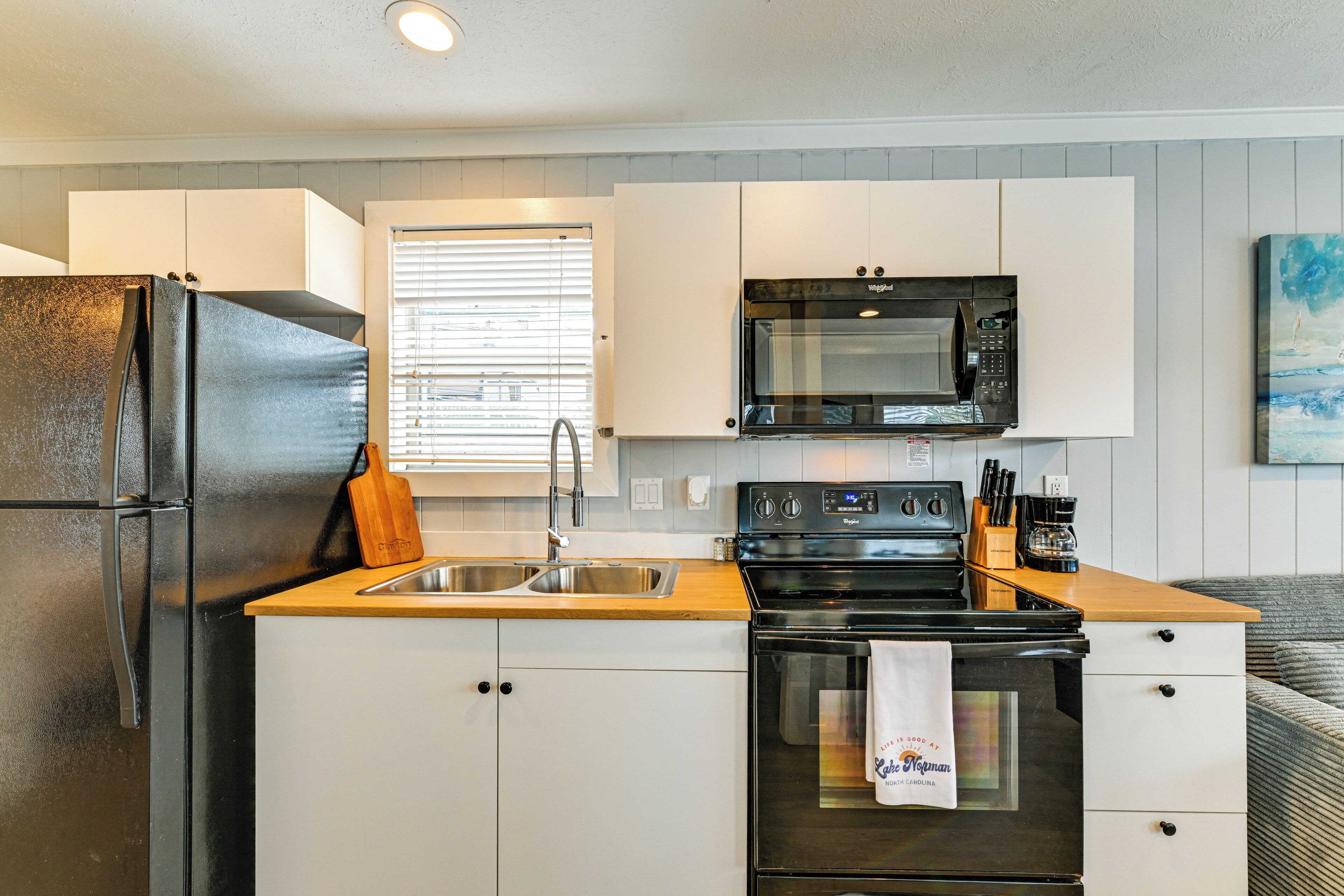 A compact kitchen with a refrigerator, sink, microwave, oven, and wooden countertop.