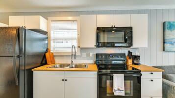 A compact kitchen with a refrigerator, sink, microwave, oven, and wooden countertop.
