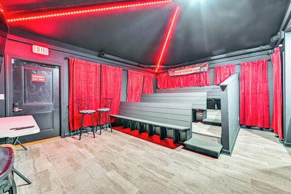 Un teatro con cortinas rojas, un letrero de salida y una zona de asientos con bancos.