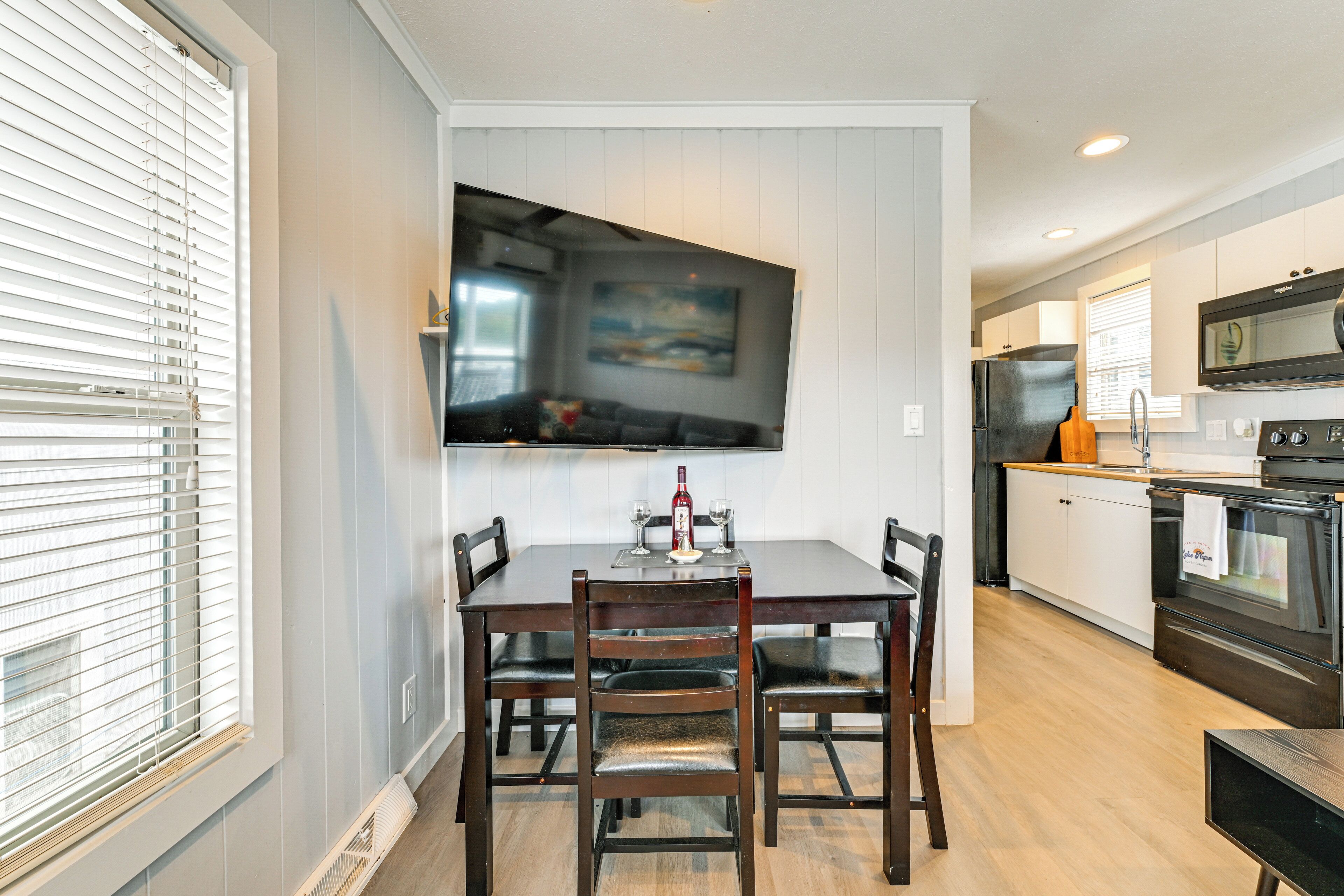 A dining area with a wooden table and chairs, a flat-screen TV mounted on the wall, and a kitchen with modern appliances.