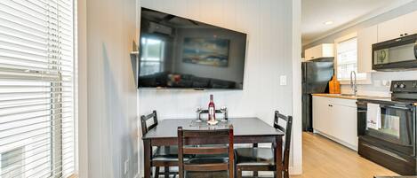 A dining area with a wooden table and chairs, a flat-screen TV mounted on the wall, and a kitchen with modern appliances.