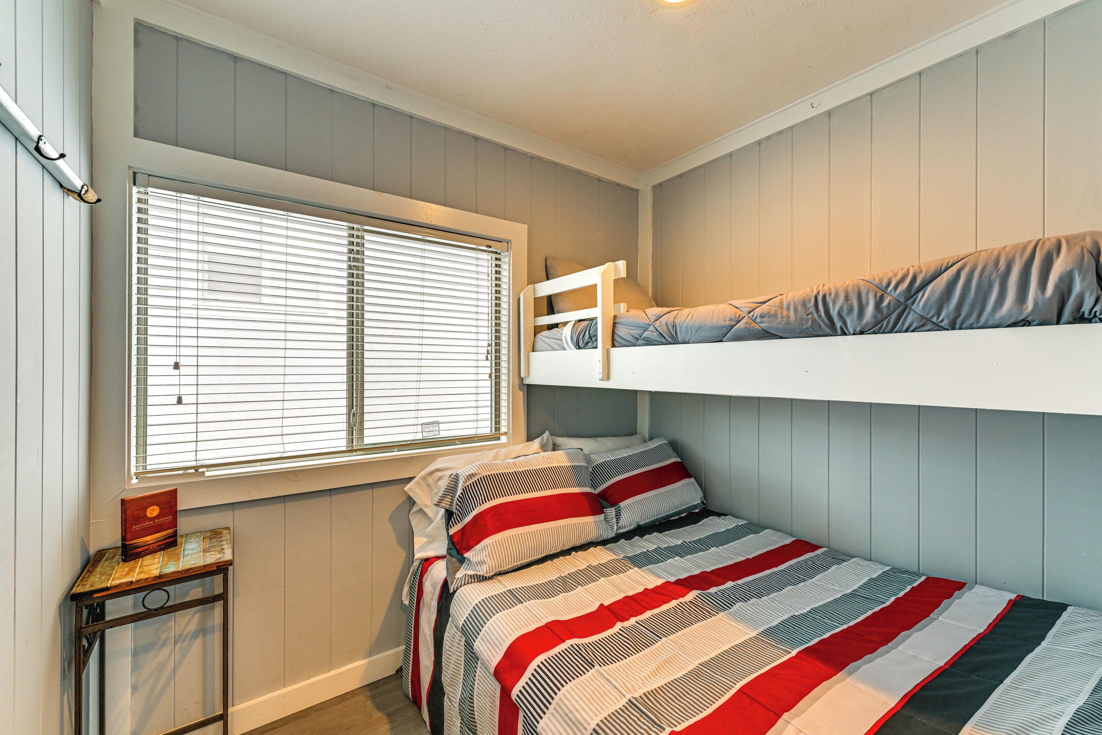 A bunk bed with striped bedding, a window with blinds, and a small table with a book.