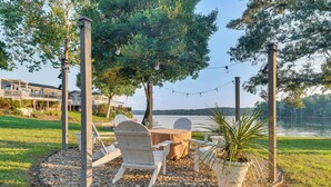 An outdoor seating area with chairs and a table, surrounded by pebbles, with a view of a lake and houses in the background. - Breathtaking Lake Views and Sunsets on Badin Lake! (New London)