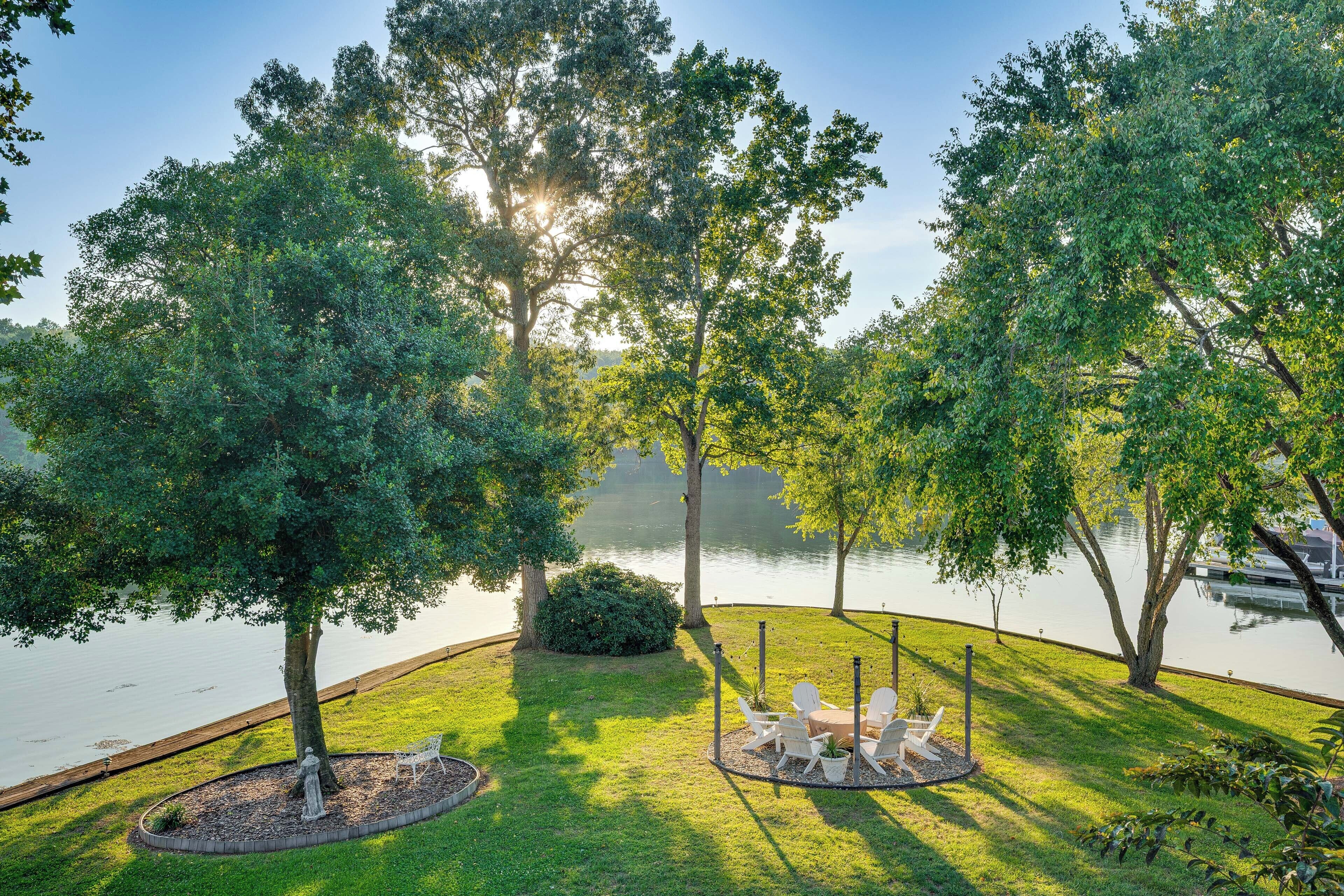 A serene lakeside patio with a circular seating area, surrounded by lush greenery and trees.