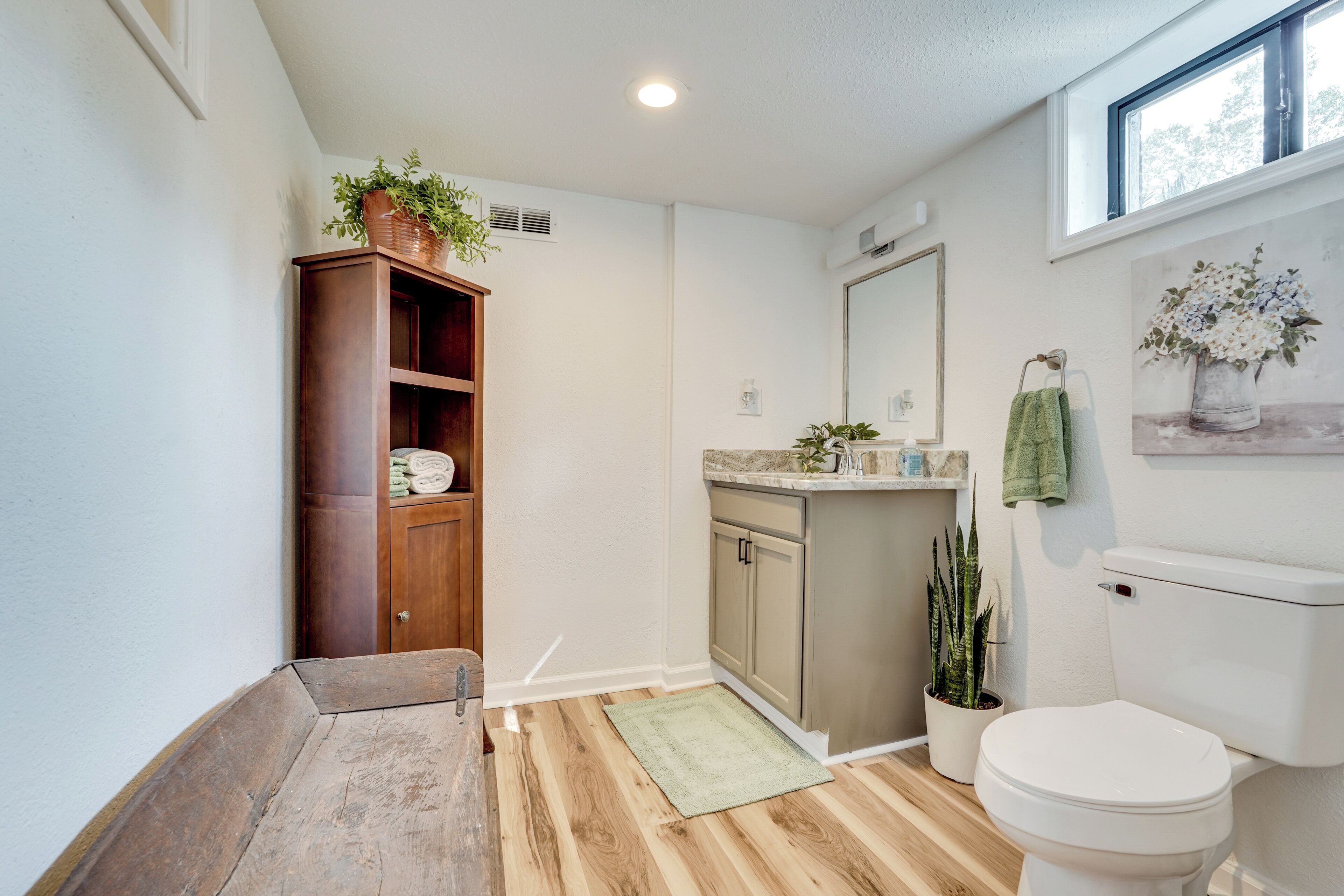 A bathroom with wooden flooring, a toilet, a sink with a mirror, and a potted plant.