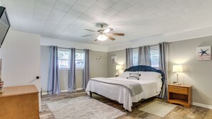 Ein Schlafzimmer mit einem Bett, Nachttischen, einem Deckenventilator und einem Fenster mit Vorhängen.