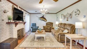Ein Wohnzimmer mit Kamin, Fernseher, einer Kristallleuchter und einem großen Wandbild mit Fischen.