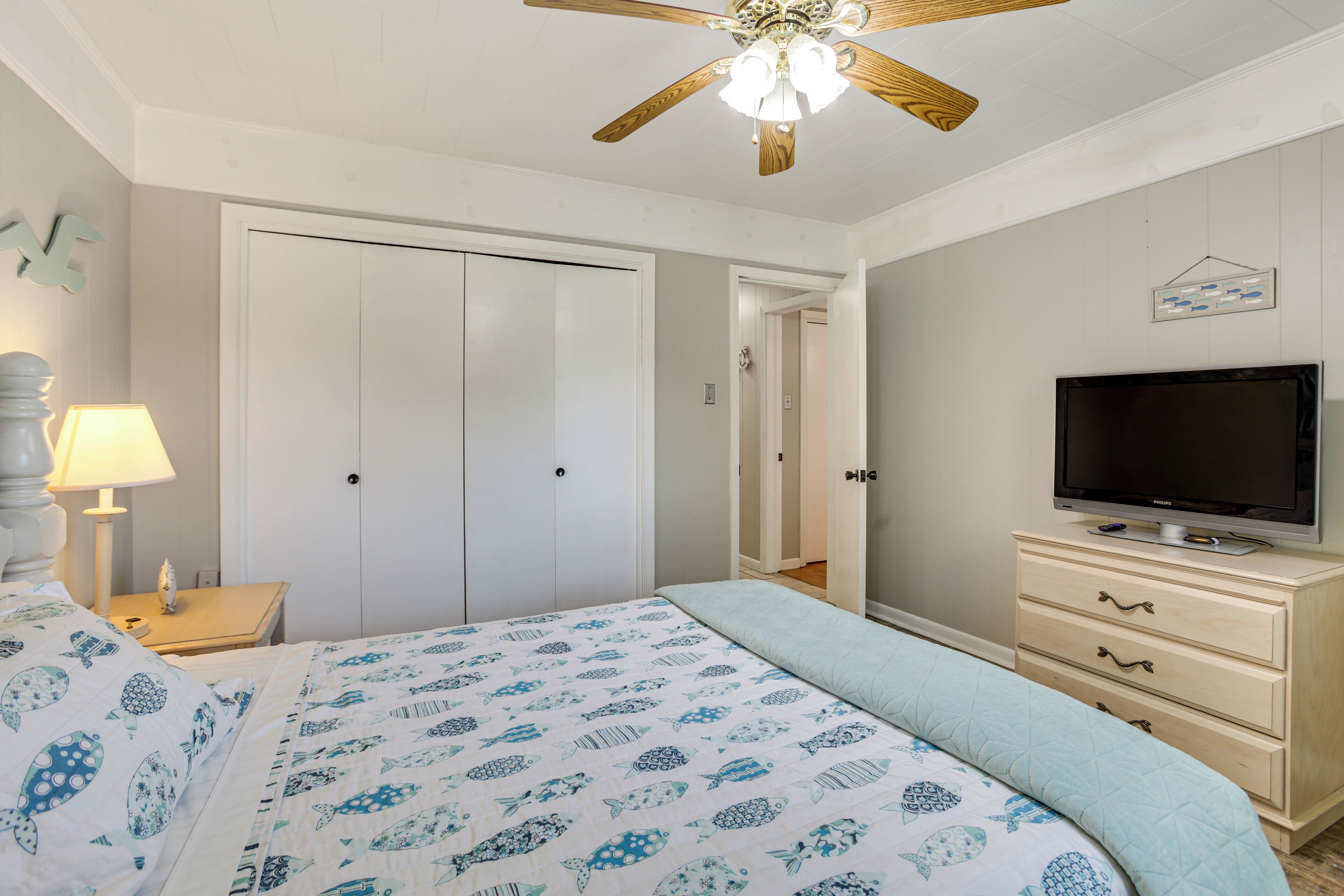 A bedroom with a bed, a television on a dresser, a ceiling fan, and a door.