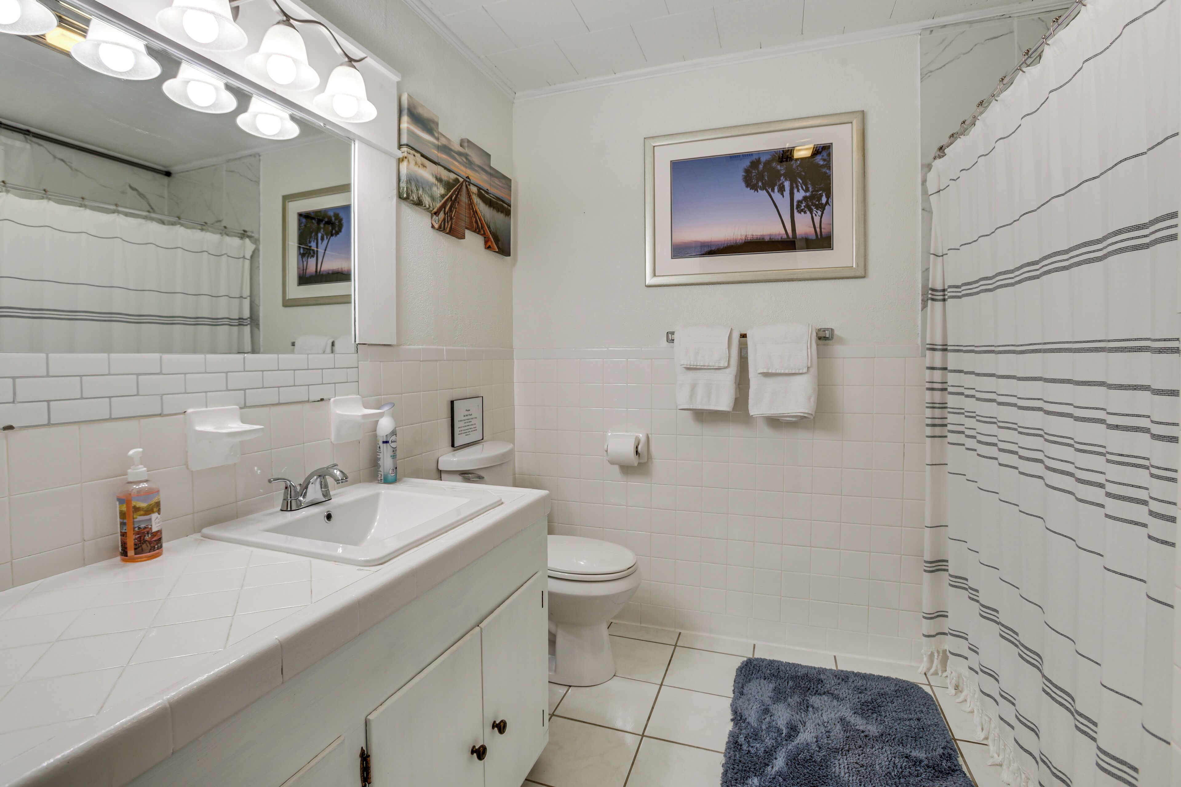 Ein Badezimmer mit weißem Waschbecken, Spiegel und Toilette, einem blauen Handtuch und einem Duschvorhang mit Streifenmuster.