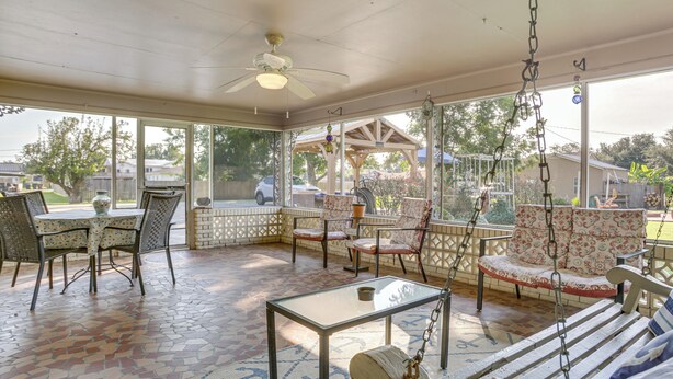 Eine überdachte Terrasse mit Tisch, Stühlen, einer Schaukel und einem Deckenventilator.