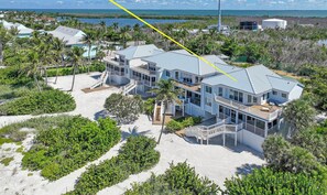Il s’agit d’une vaste propriété moderne située en bord de mer, comprenant plusieurs bâtiments, dont une maison principale et des dépendances, le tout entouré d’une végétation luxuriante et bordé d’une plage de sable.