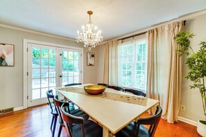 A dining room with a wooden table, chairs, a chandelier, and a large window with curtains. - Clinton Retreat Near Norris Lake & Knoxville (Clinton)