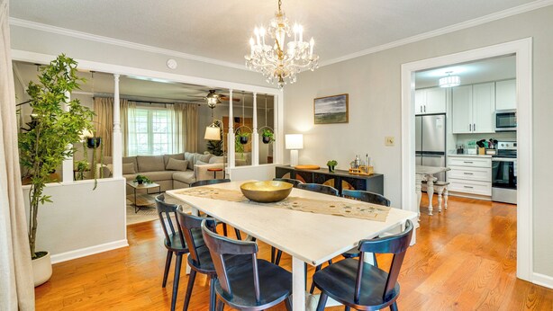 Un espace repas comprenant une grande table, des chaises, un lustre et donnant sur le salon.