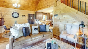 Un intérieur de chalet chaleureux avec un canapé en cuir, un coin repas et un escalier menant à une mezzanine.