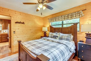 A wooden-paneled bedroom with a bed, a ceiling fan, a window with curtains, and a nightstand with a lamp. - Deck, Panoramic Views: Serene Mineral Bluff Cabin! (Mineral Bluff)