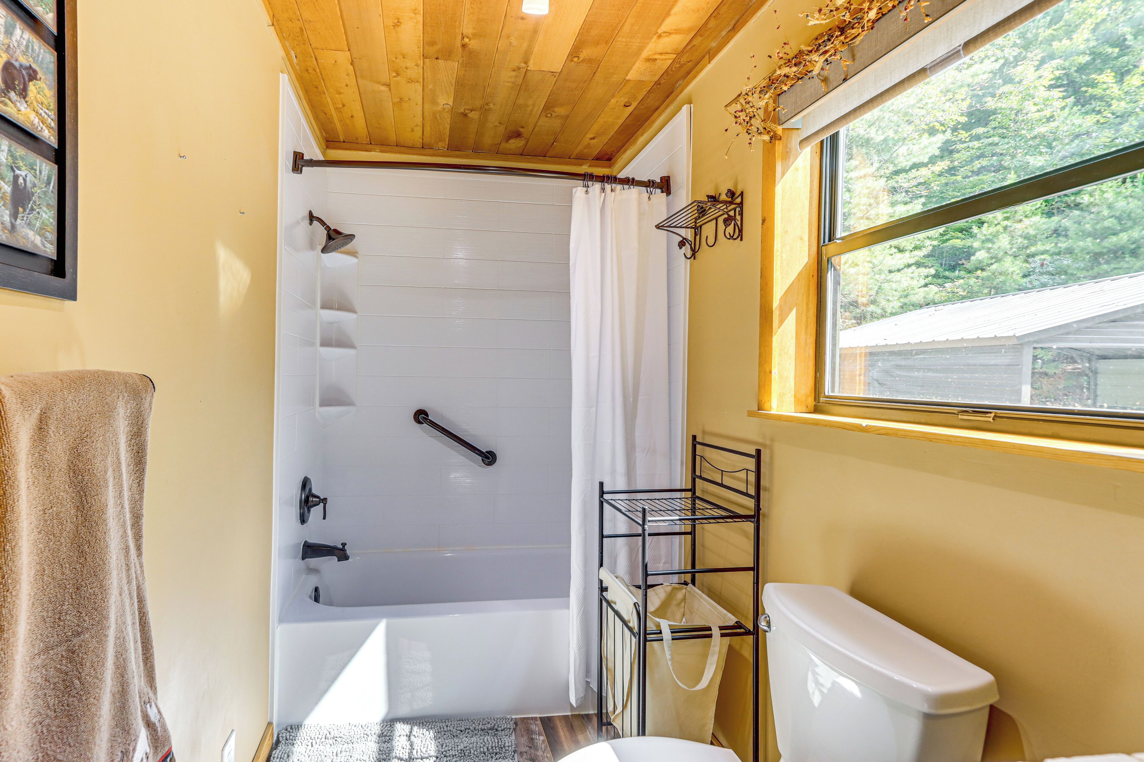 A bathroom with a bathtub, toilet, and a window with a view of trees.