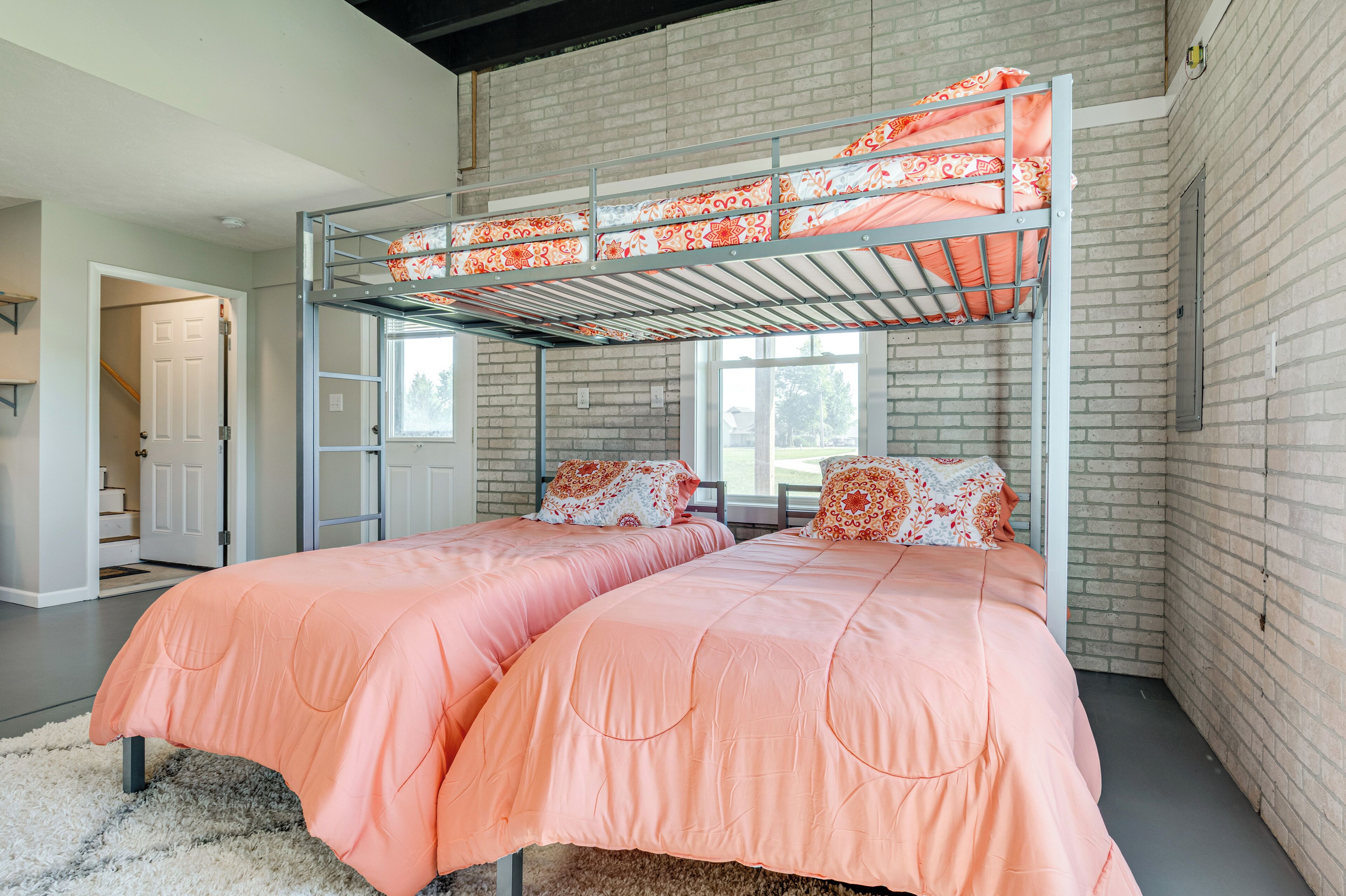 A room with a bunk bed, two single beds, and a large window.