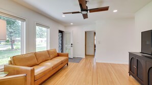 A modern living room with a leather sofa, wooden flooring, a ceiling fan, and a TV on a cabinet. - Pet-friendly Minneapolis Home w/ Spacious Yard (Golden Valley)