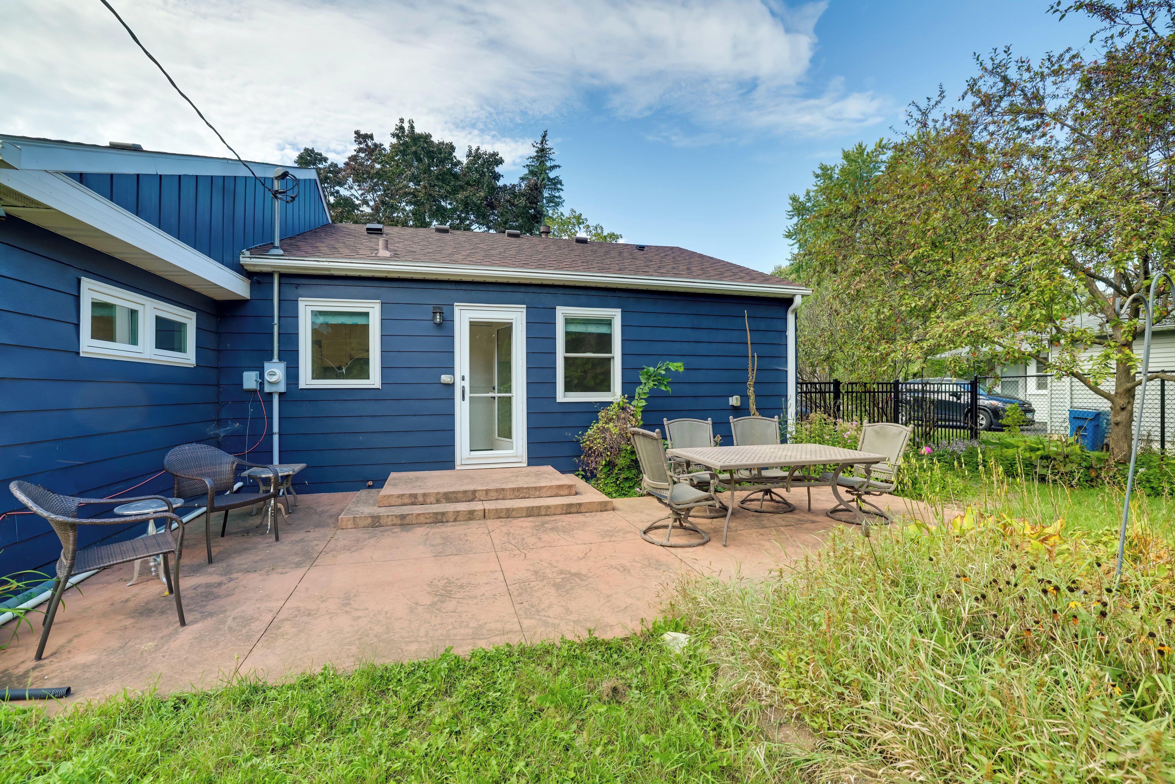 A residential house with a blue exterior, a front door, and a patio area with outdoor furniture.