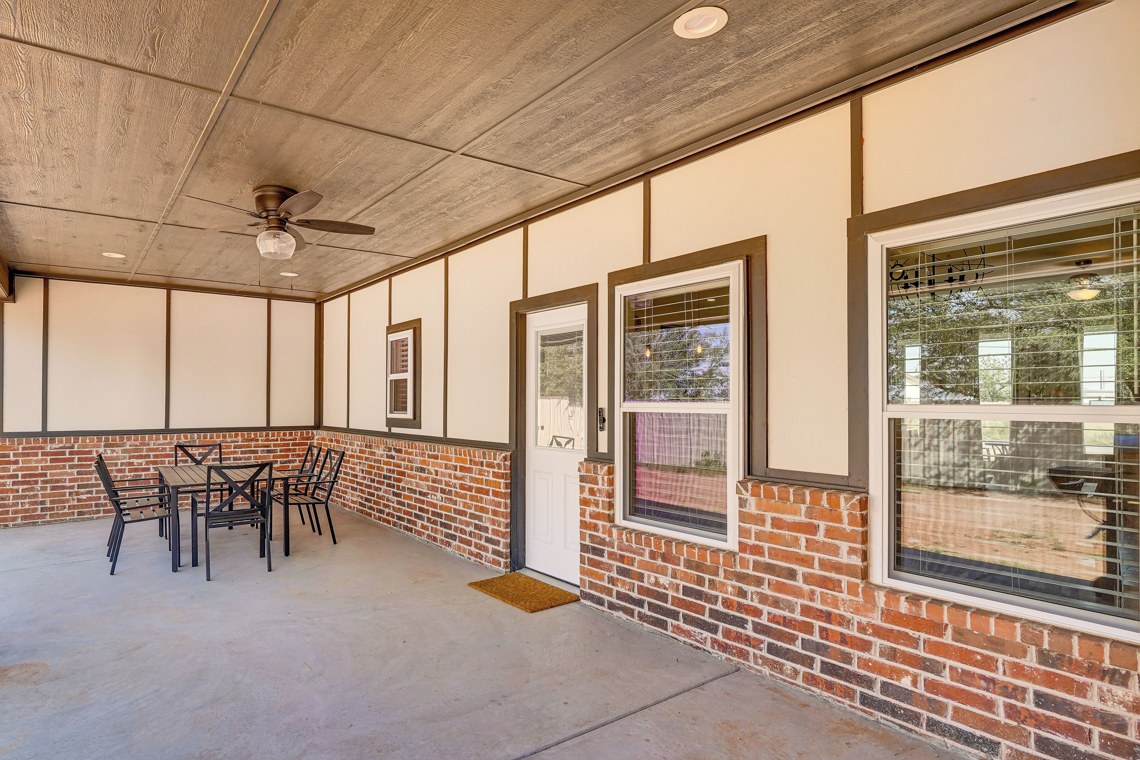 A covered patio area with a brick wall, a ceiling fan, and a table with chairs.